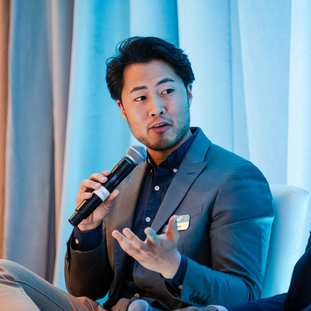 Portrait of Brian Kim speaking at a conference panel, holding a microphone